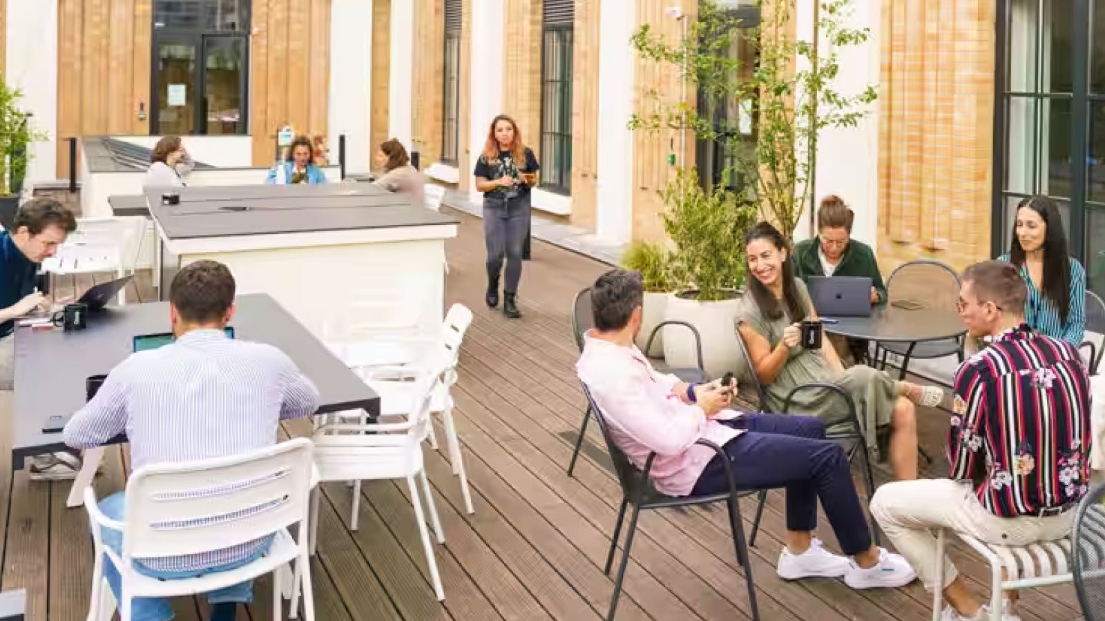 People working and collaborating in an outdoor office courtyard with laptops and seating areas beside a modern building.