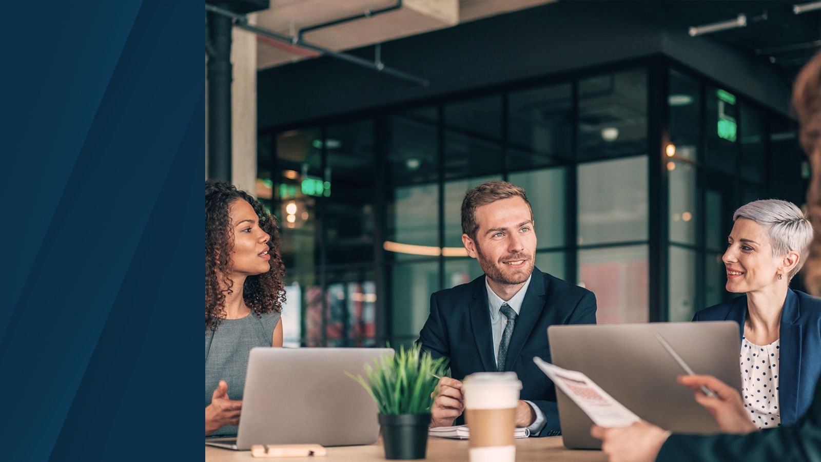 Group of professionals collaborating around a conference table with laptops, documents, and coffee cups in a modern office setting.