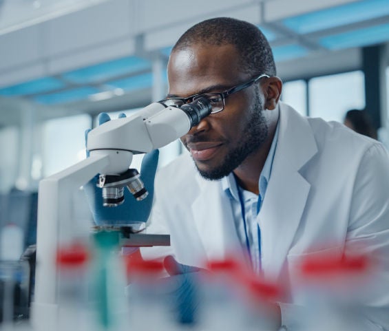 A scientist in a lab coat observes a sample under a microscope, focused on his research in a laboratory environment.