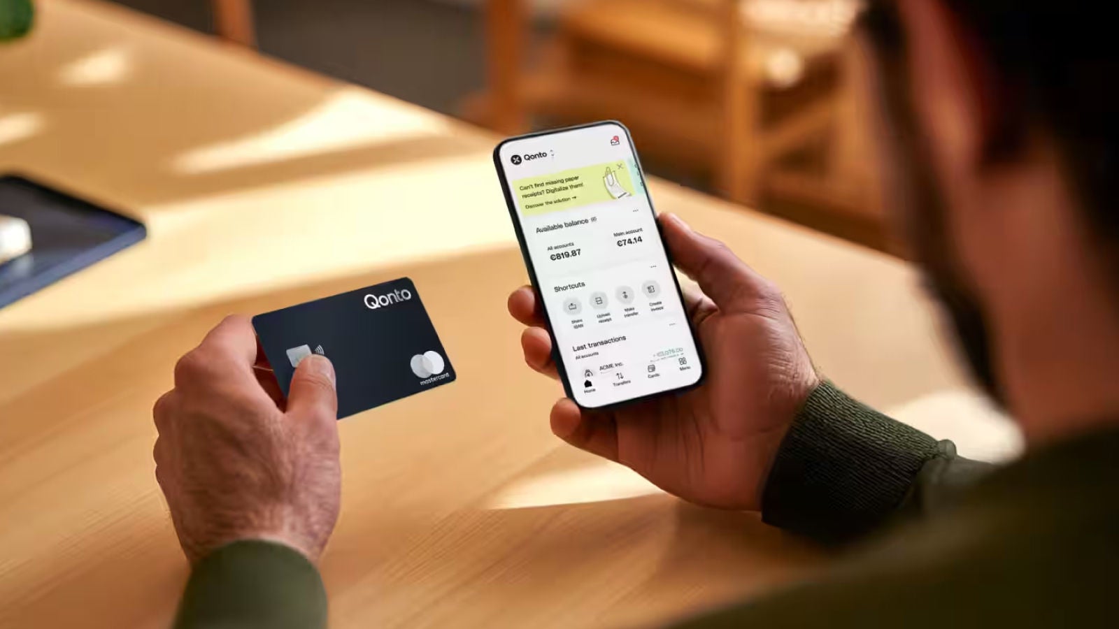 Person holding a Qonto payment card while viewing the Qonto mobile banking application on a smartphone.