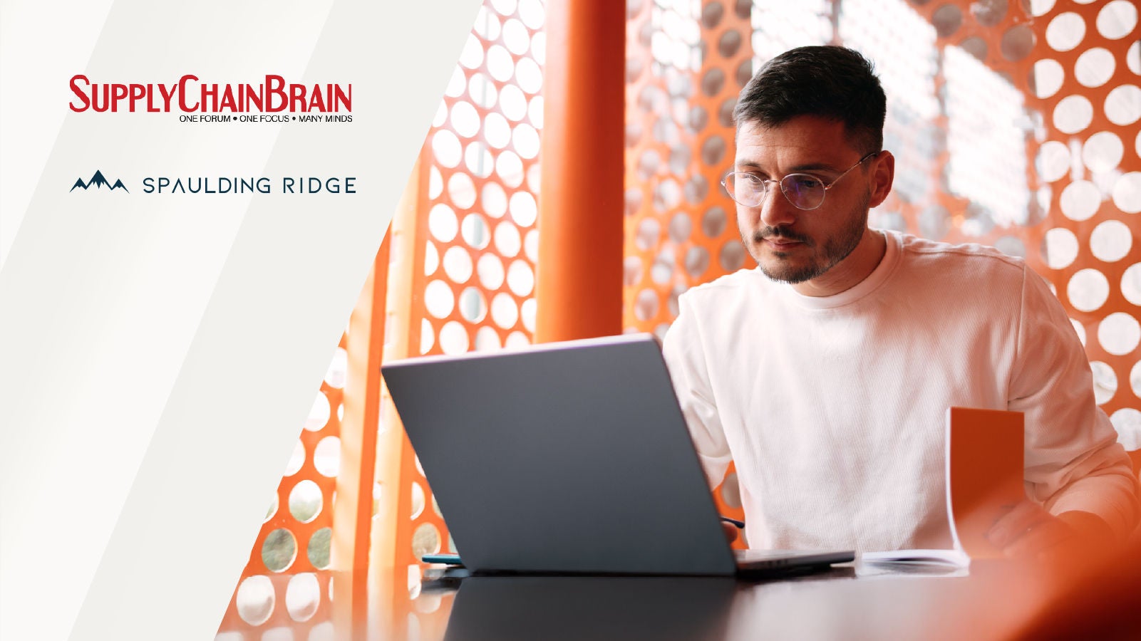 A professional focused on a laptop in a contemporary workspace with orange patterned walls, alongside the logos of SupplyChainBrain and Spaulding Ridge.