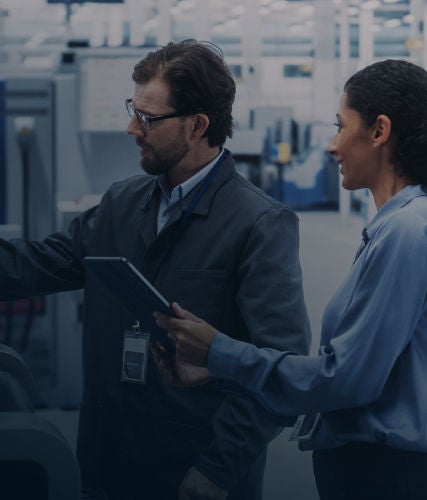 Two professionals reviewing data on a machine screen in a factory setting, alongside robotic arms assembling solar panels on an automated production line.