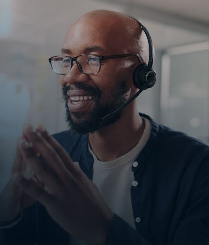 A customer service representative wearing a headset and smiling during a conversation in an office environment.