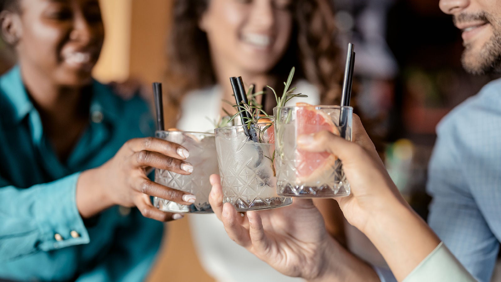 Group of people smiling and clinking glasses filled with cocktails garnished with grapefruit and rosemary.