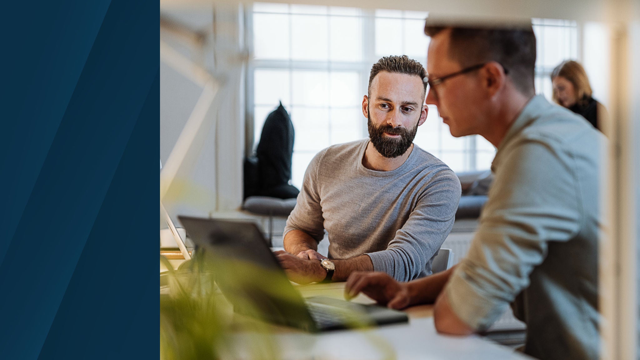 Two colleagues working together at a desk using a laptop in a modern office