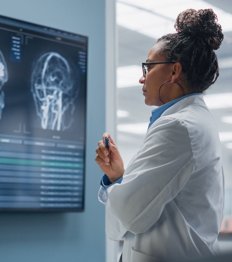 A focused doctor in a lab coat reviews brain scan images on a large monitor in a medical setting.