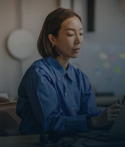 Woman working on a laptop at a desk in an office setting.