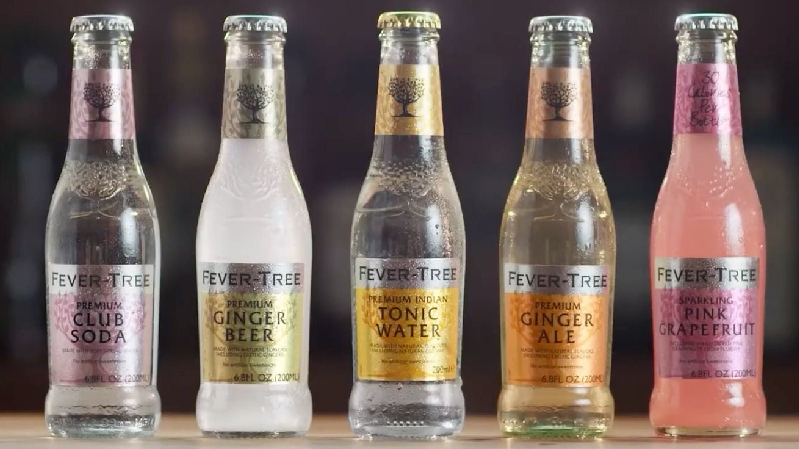 Lineup of five Fever-Tree bottles including Club Soda, Ginger Beer, Tonic Water, Ginger Ale, and Sparkling Pink Grapefruit, displayed with condensation.