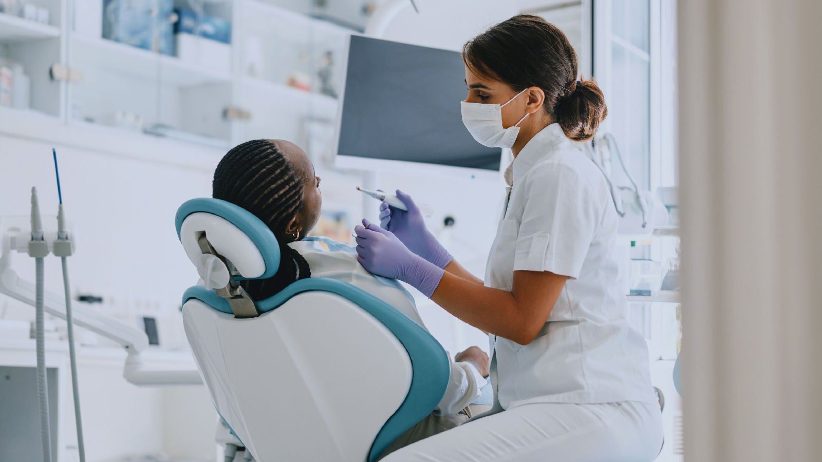 Image showing a dentist wearing a mask and gloves treating a patient in a dental chair inside a clinic.