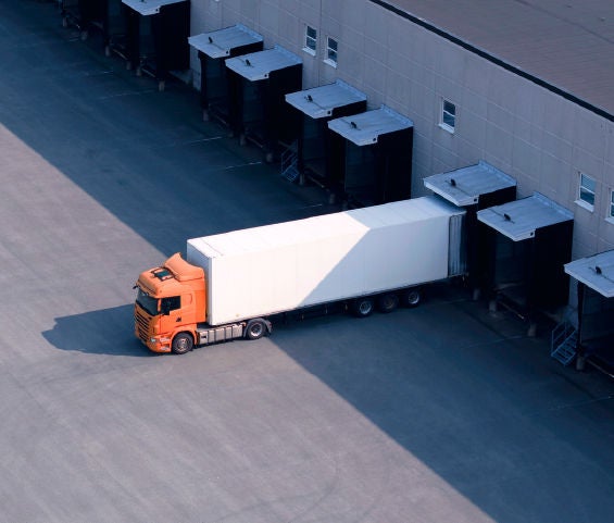 An orange truck parked in front of a large warehouse, showcasing its vibrant color against the industrial backdrop.