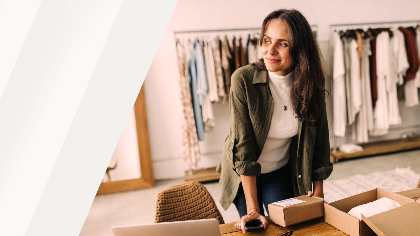 Une professionnelle du retail debout devant une table avec des colis à l’intérieur d’un magasin de vêtements, avec des portants de vêtements visibles en arrière-plan.