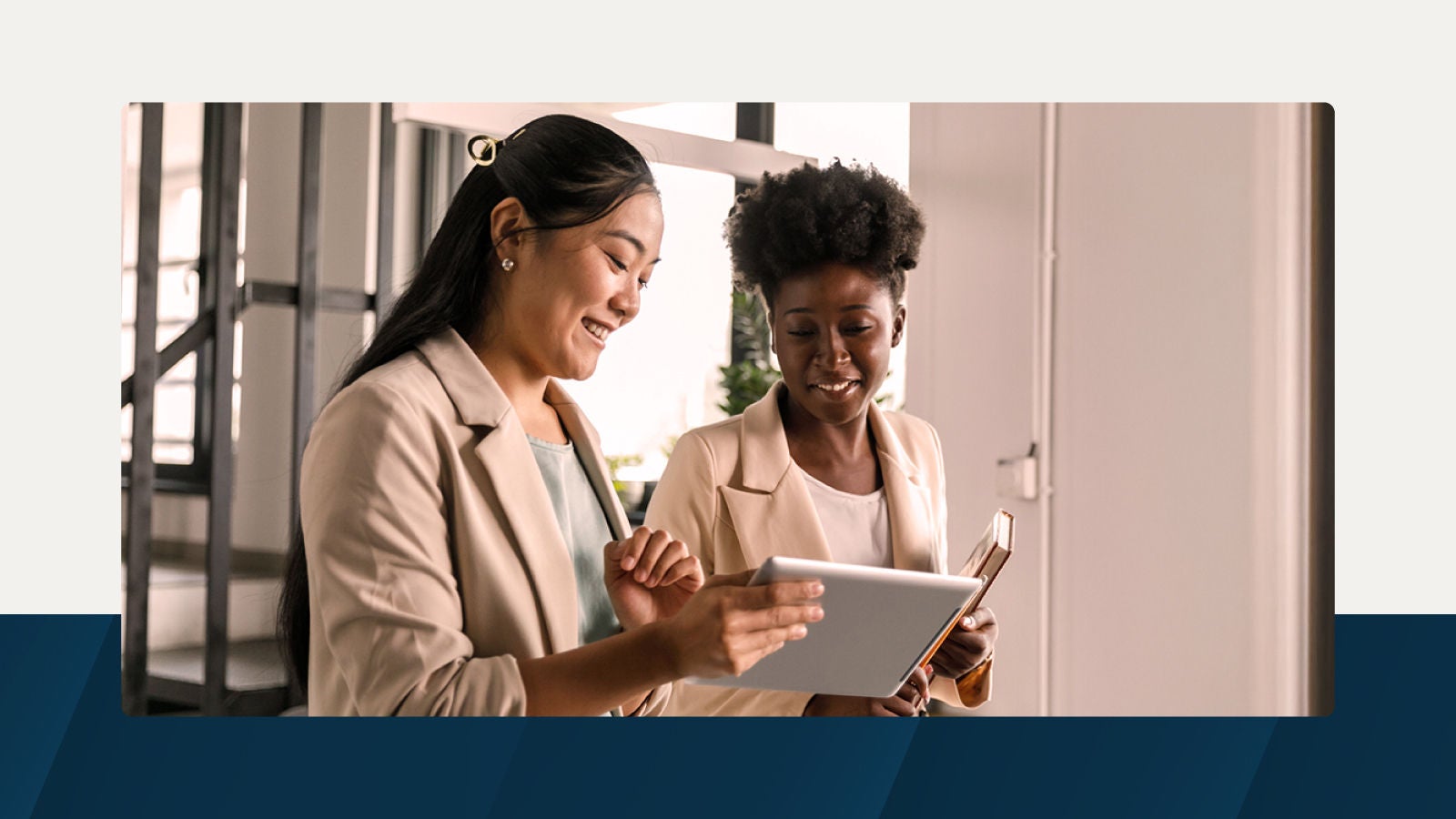 Two professionals smiling and collaborating while using a tablet, standing in a modern office environment.