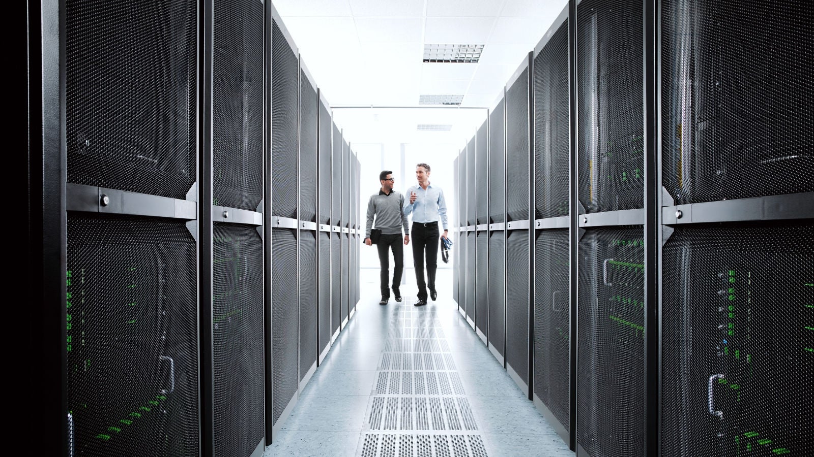 Two professionals walking between rows of server racks in a data center.
