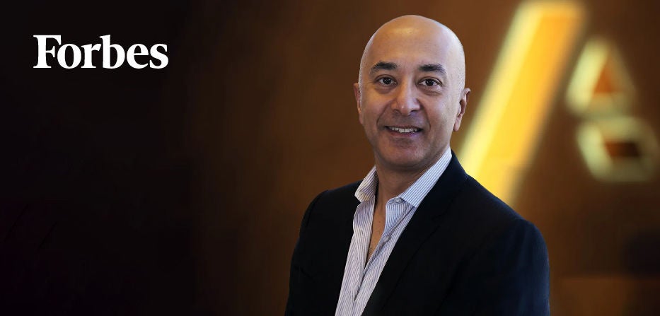 Forbes feature with a portrait of a man in a suit smiling, standing in front of a blurred background with the Anaplan logo.