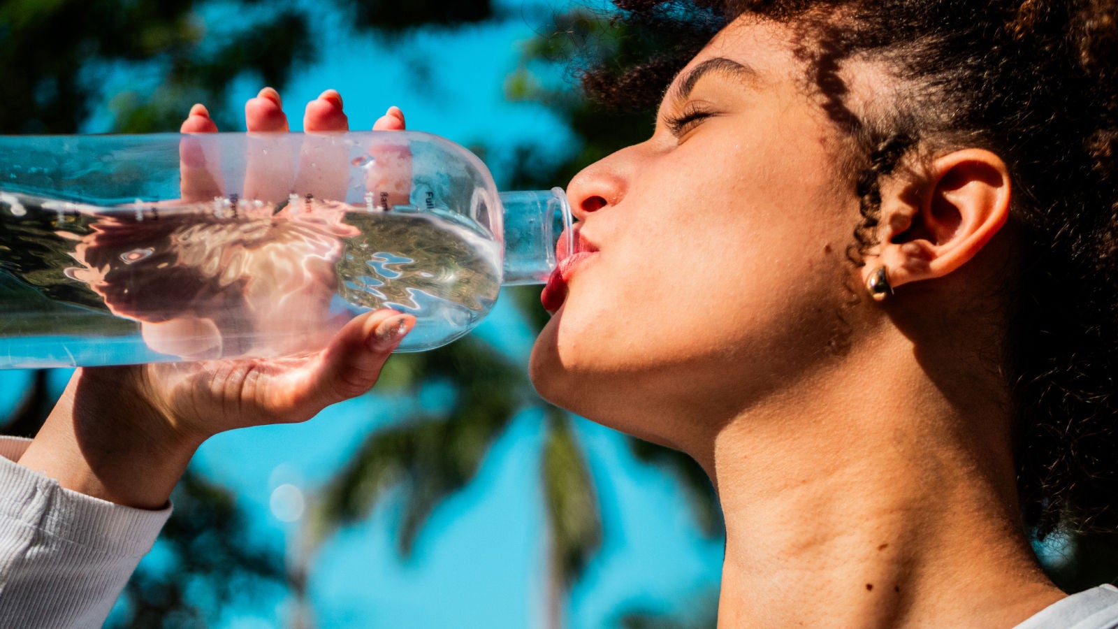 Person drinking water from a reusable bottle outdoors.