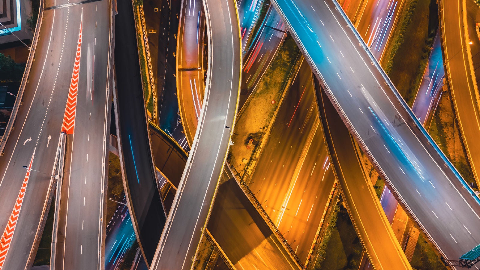 Aerial view of multiple intersecting highways at night, lit with blue and orange lights, representing the complexity and interconnectivity of supply chain operations.