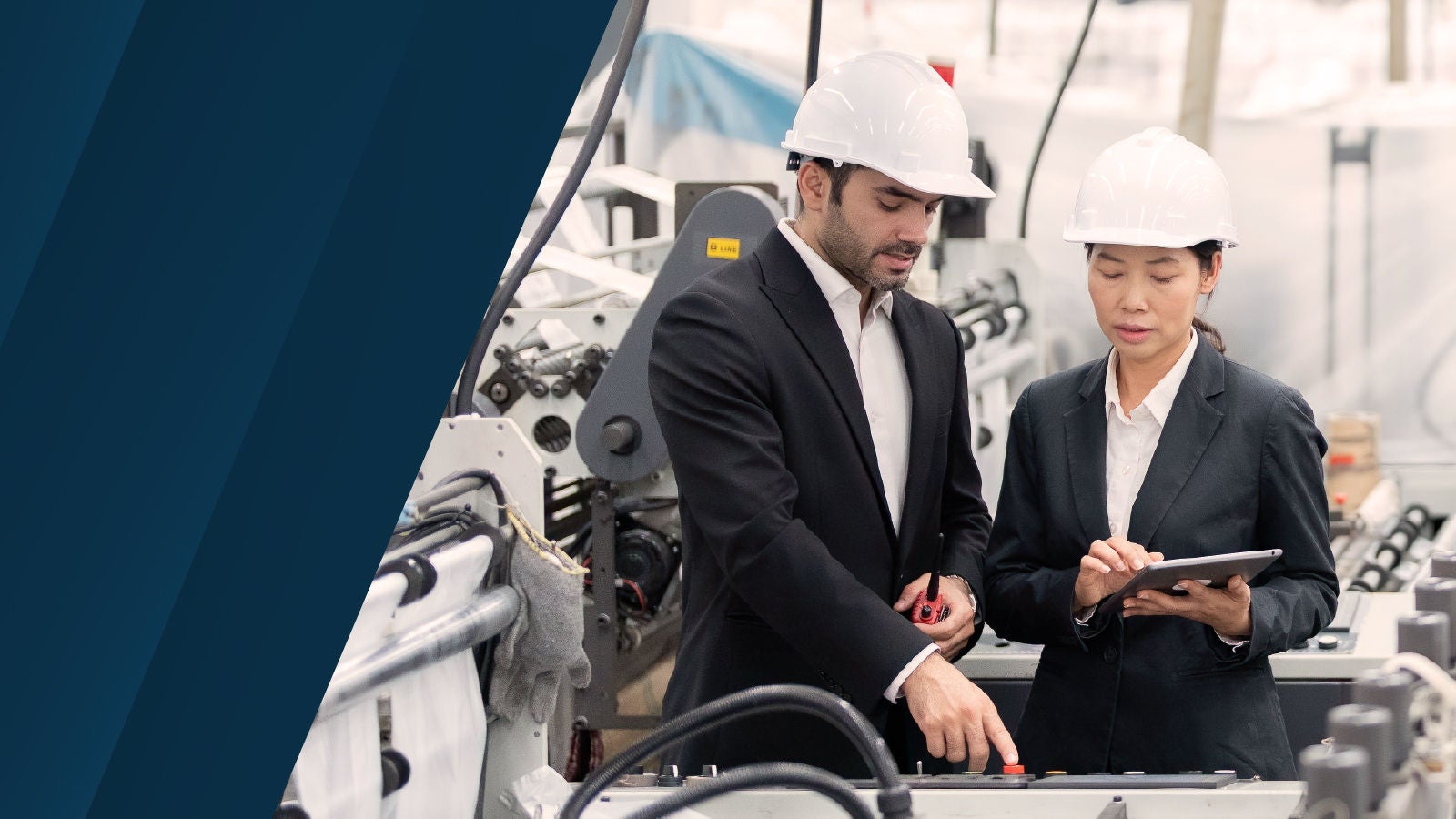 工場内でヘルメットを着用した2人が機械設備の前でタブレットを確認している様子。