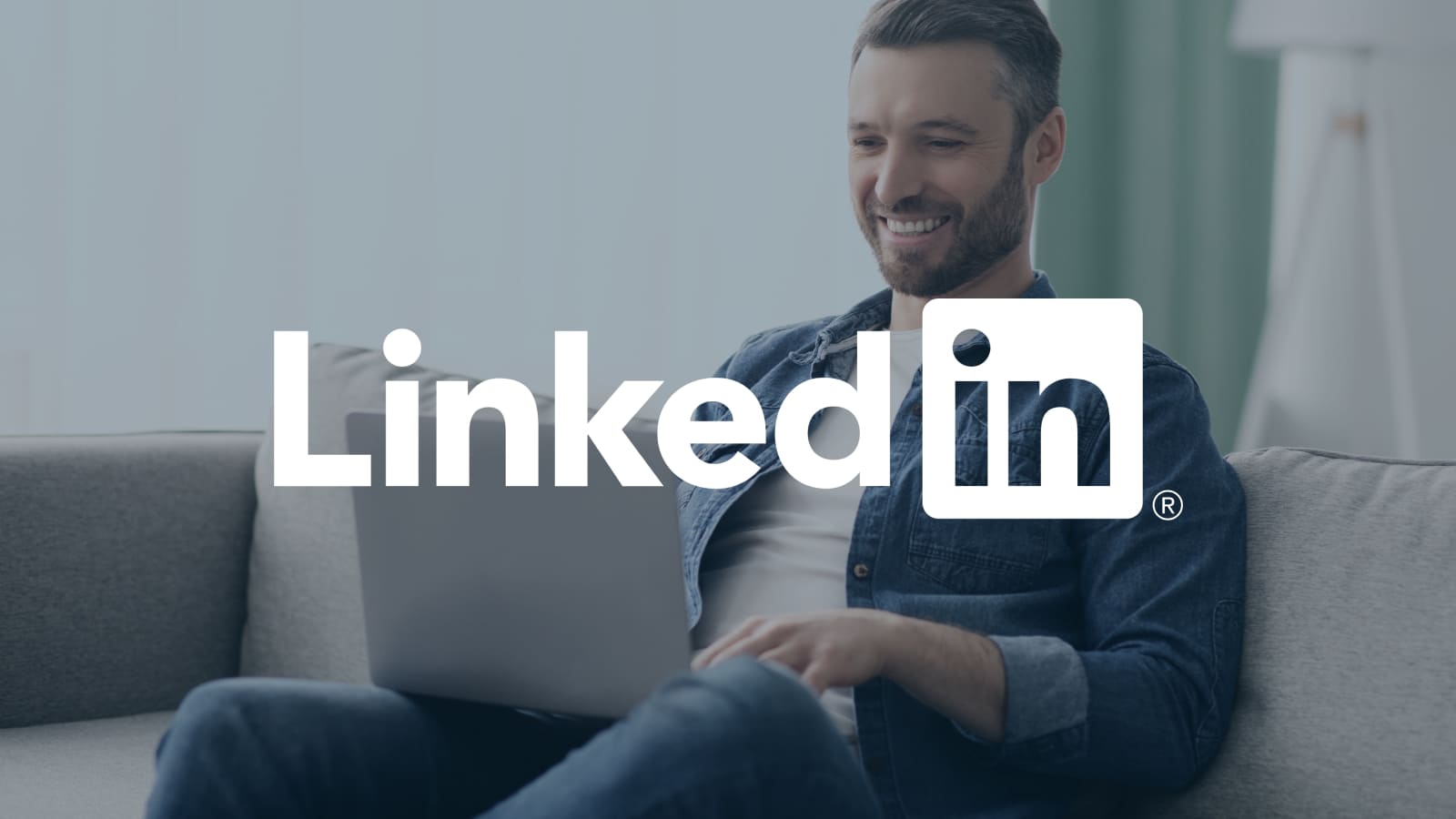 LinkedIn Logo displayed center. A man sitting on a sofa using a laptop, in a softly lit living room.