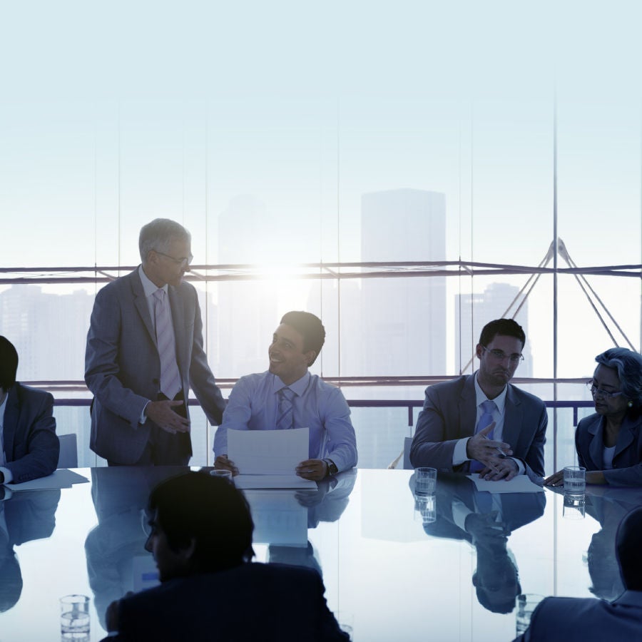 A group of business professionals engaged in a discussion within a modern meeting room setting.