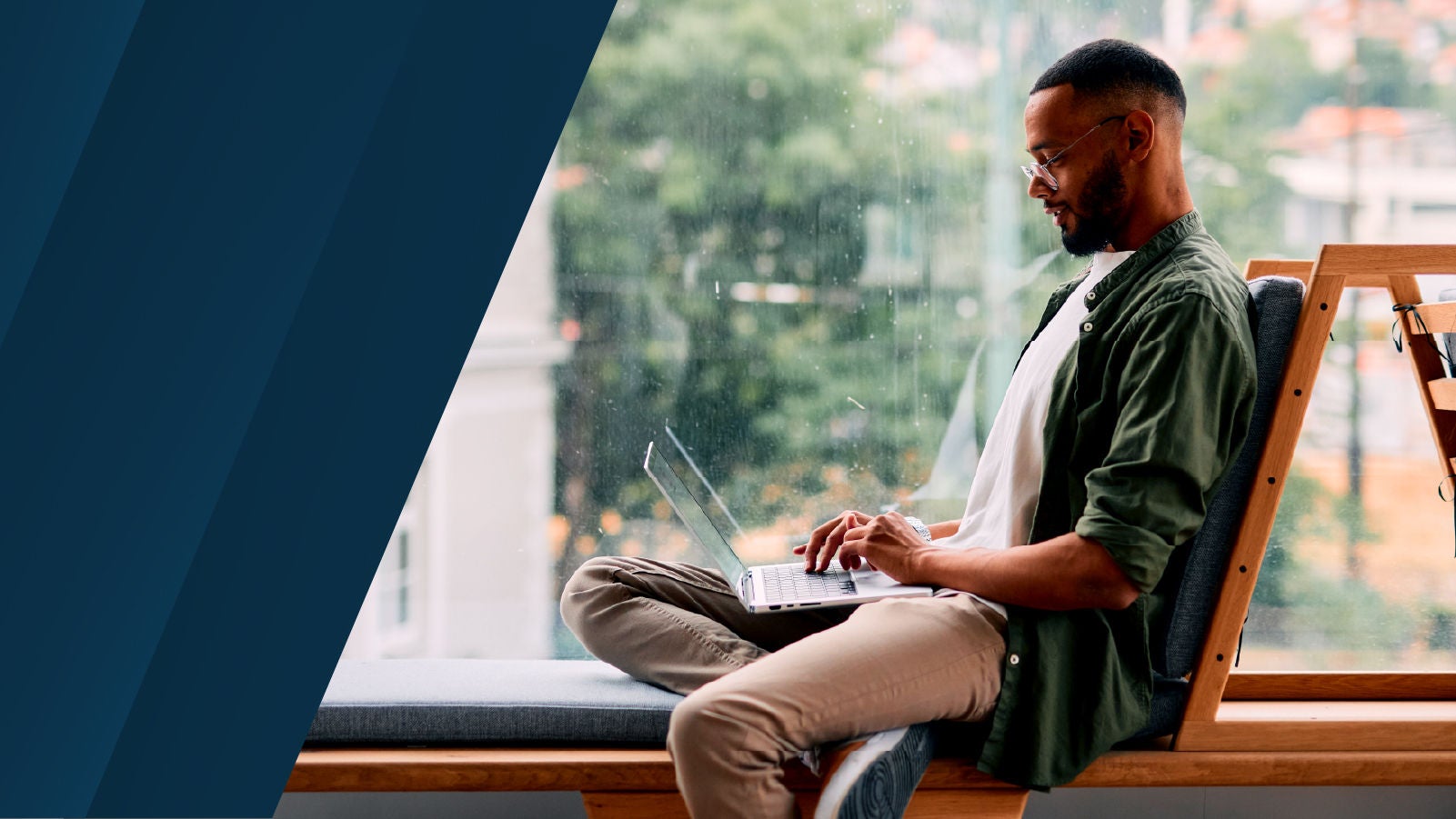 Person seated by a window working on a laptop.