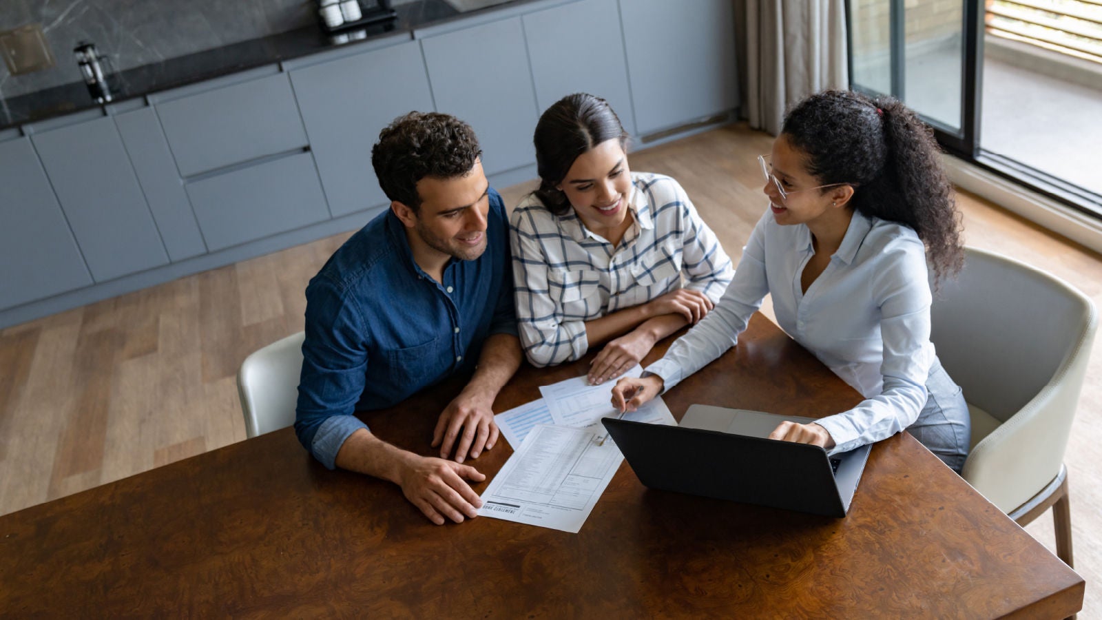 Two women and a man discussing business at a table over a laptop and papers