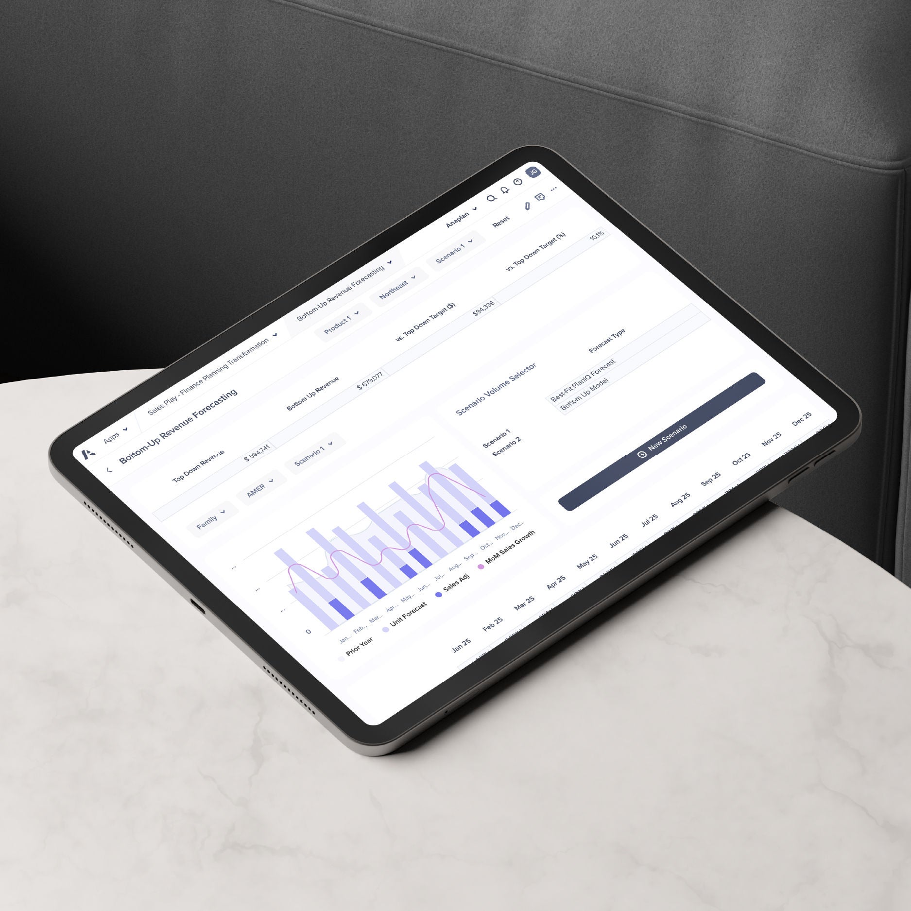 A tablet placed on a marble surface displays the Anaplan interface showing a bottom-up revenue forecasting dashboard with charts, scenario selectors, and sales growth data visualization.