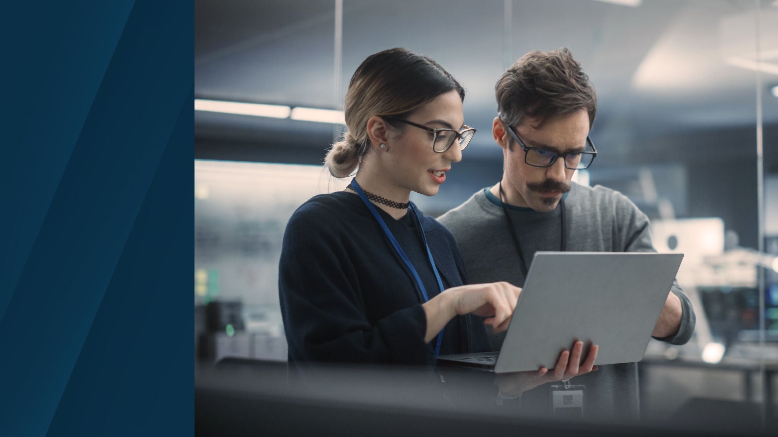 Two colleagues collaborating in a modern workspace while reviewing information on a laptop.