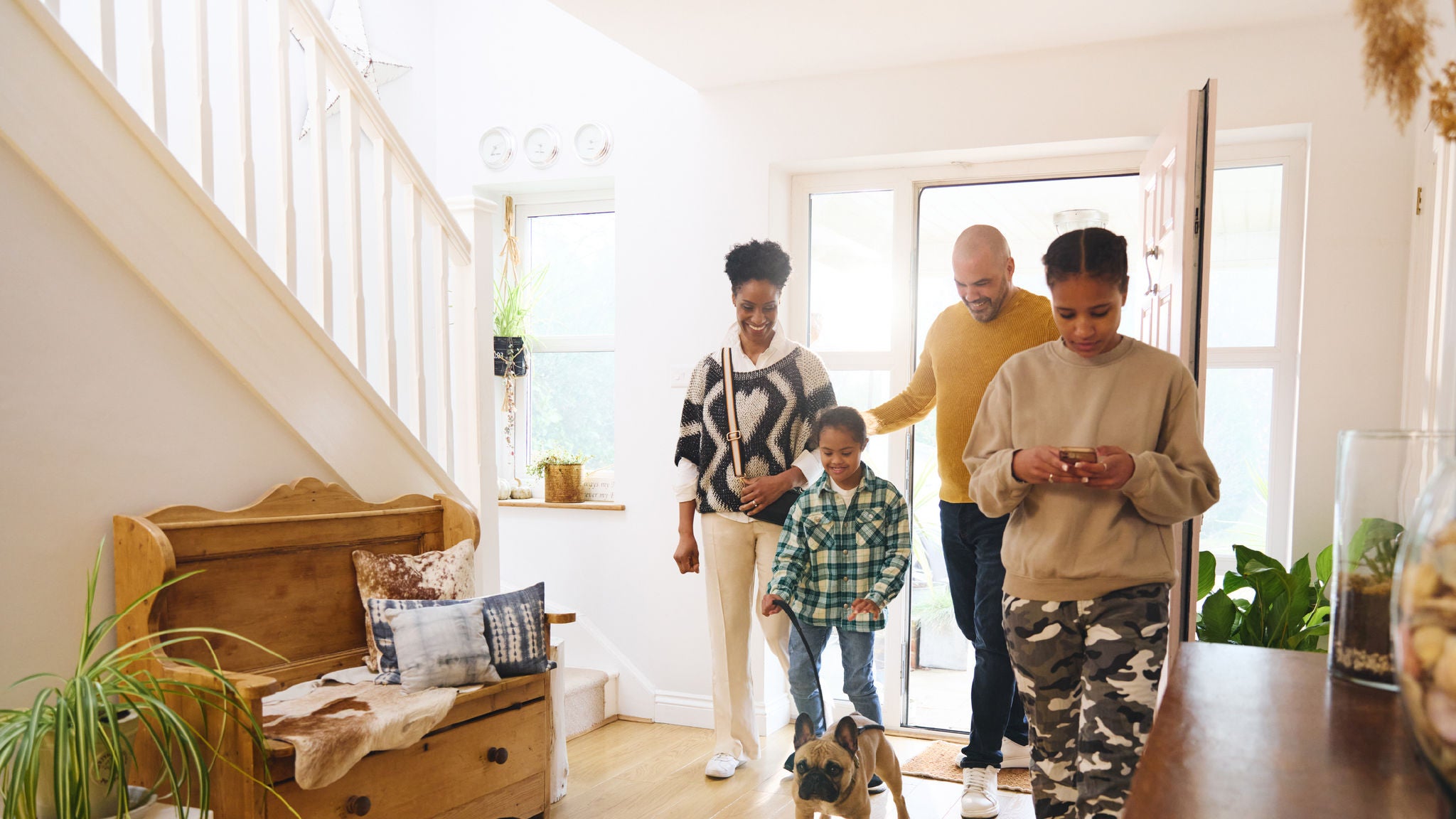 A family entering a home with a dog walking ahead in a bright entryway.
