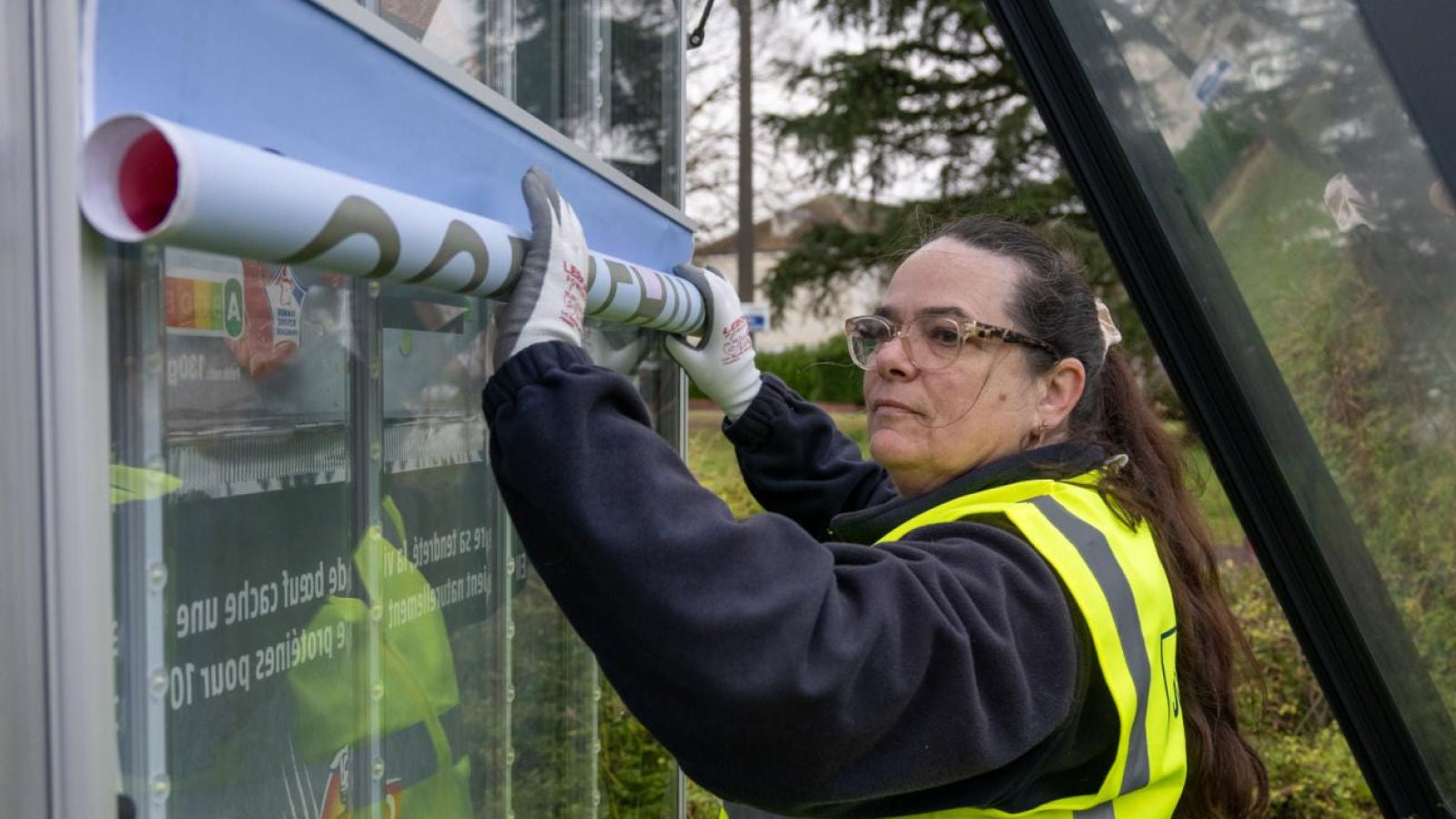 Worker in a high-visibility vest installing an advertisement on an outdoor display.