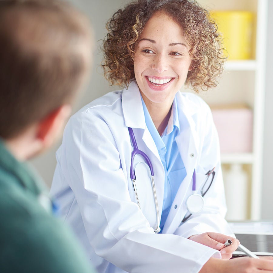 A woman speaks with a man in a doctor's office, highlighting a patient-doctor interaction.