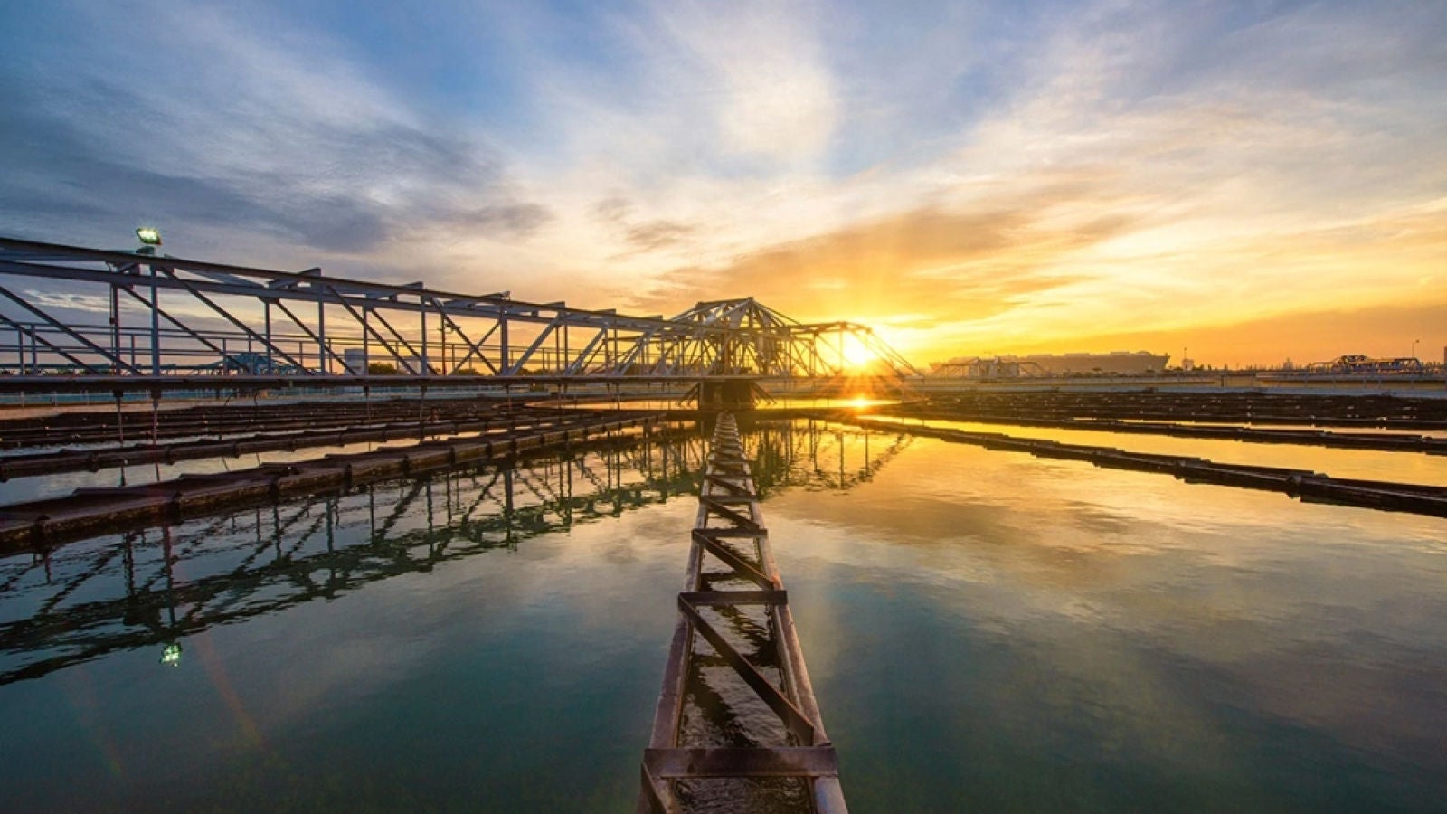 Water treatment facility with large basins and metal structures at sunset.