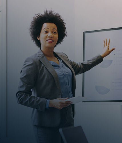 A woman presenting information on a display screen while holding a document in a meeting room.