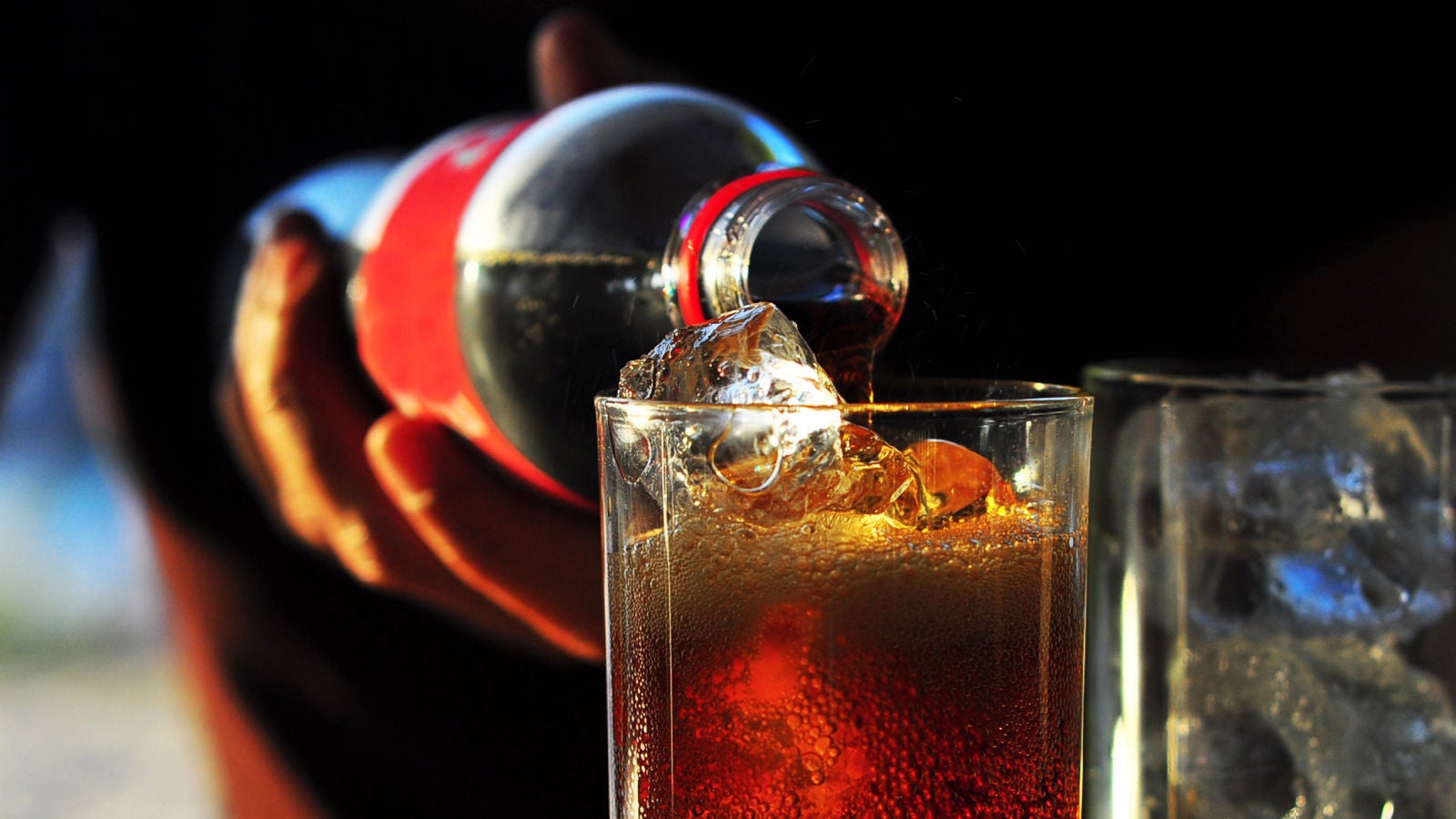 Coca-Cola pouring into a glass filled with ice