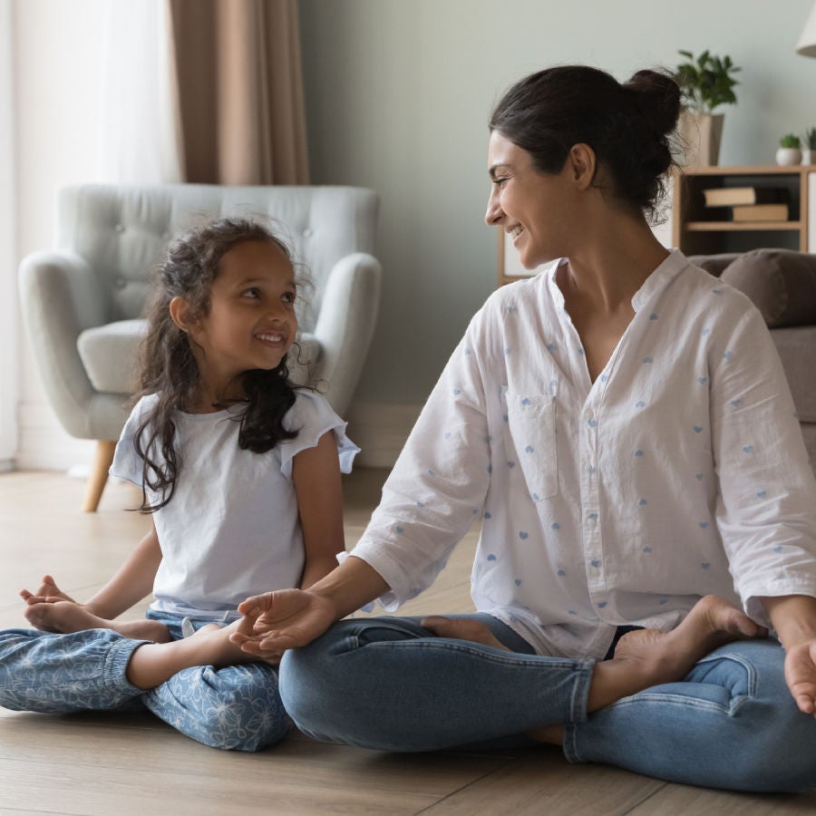 A woman and a little girl engaged in a yoga pose, sitting peacefully on a mat in a serene environment.