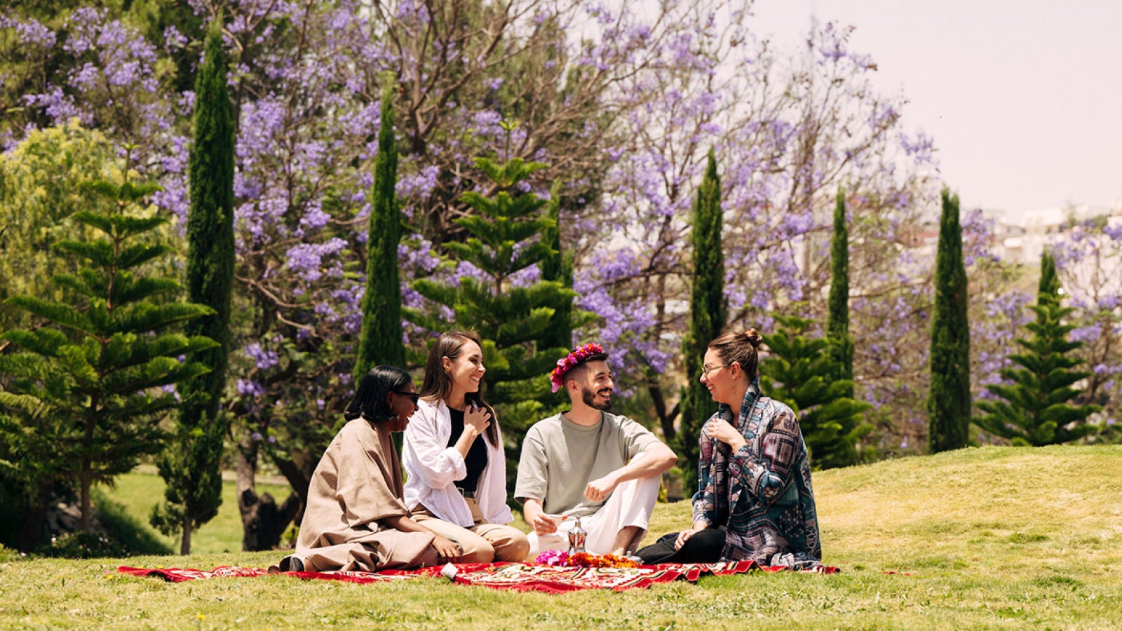 Four people sitting together on a blanket in a flowering park.