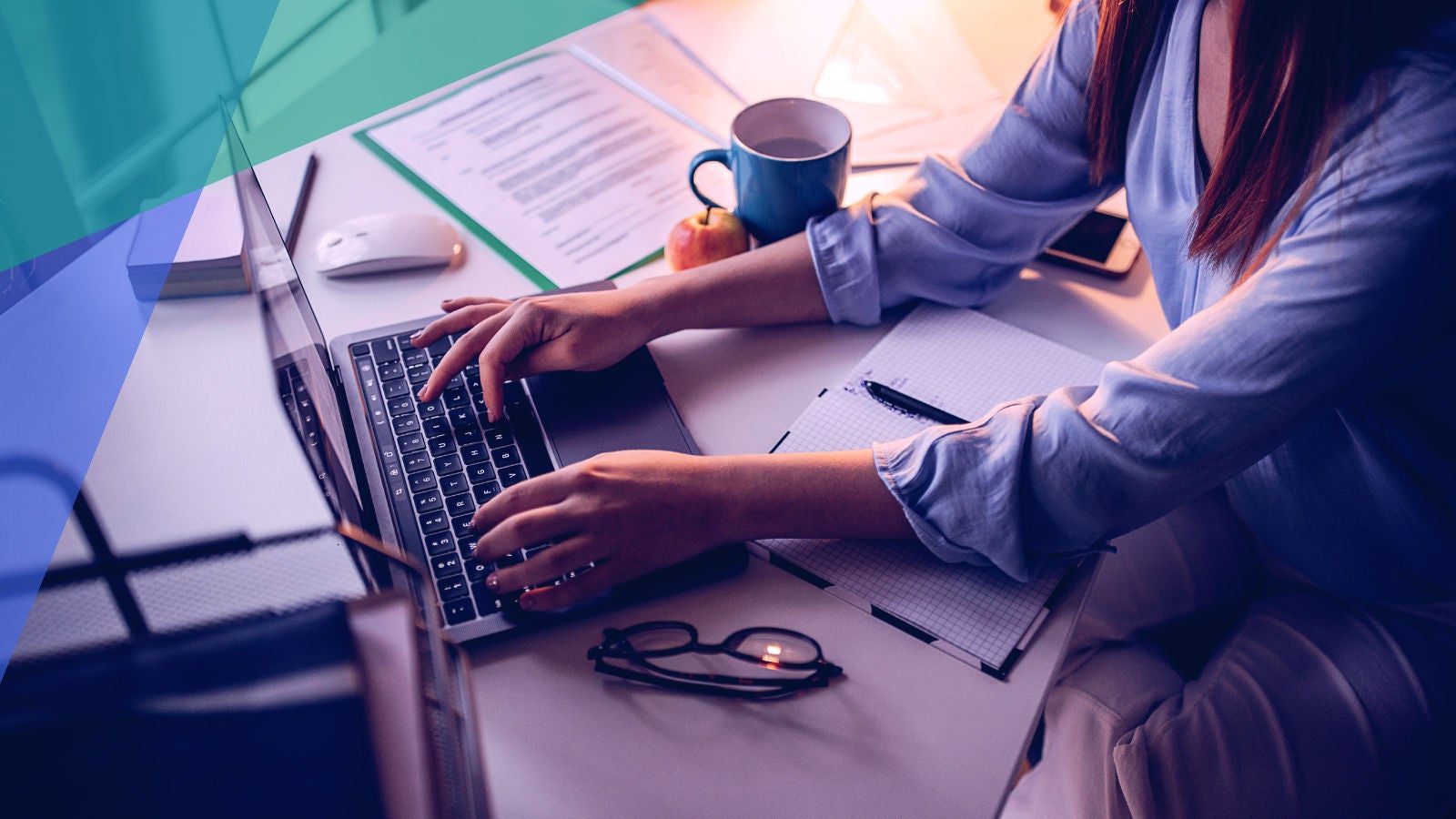 woman working on a computer surrounded by paperwork and a coffee cup