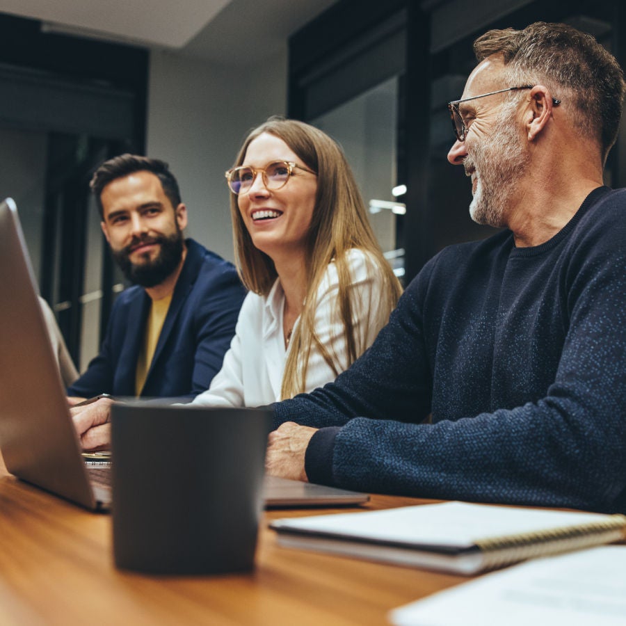 A group of three people seated at a table, collaborating with a laptop placed among them.