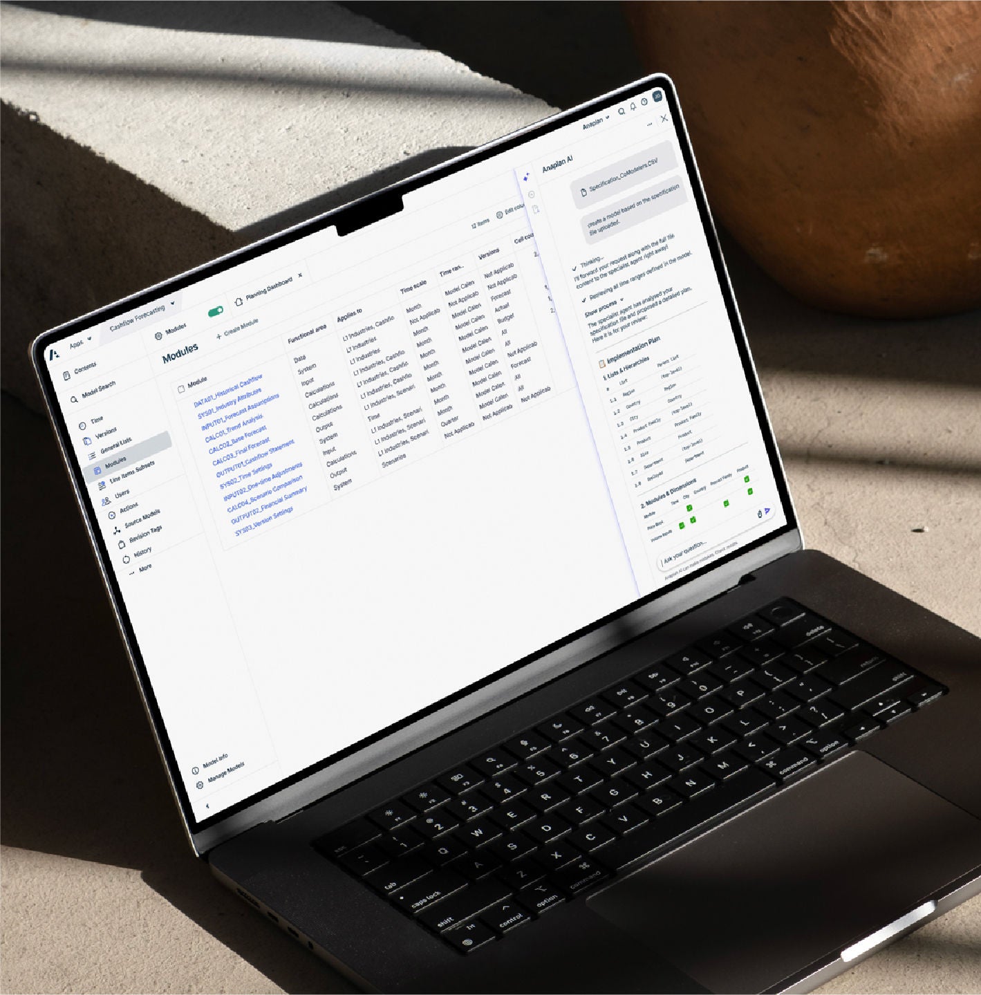 Open laptop displaying Anaplan modules and the Anaplan AI assistant on a sunlit surface beside a wooden vase.