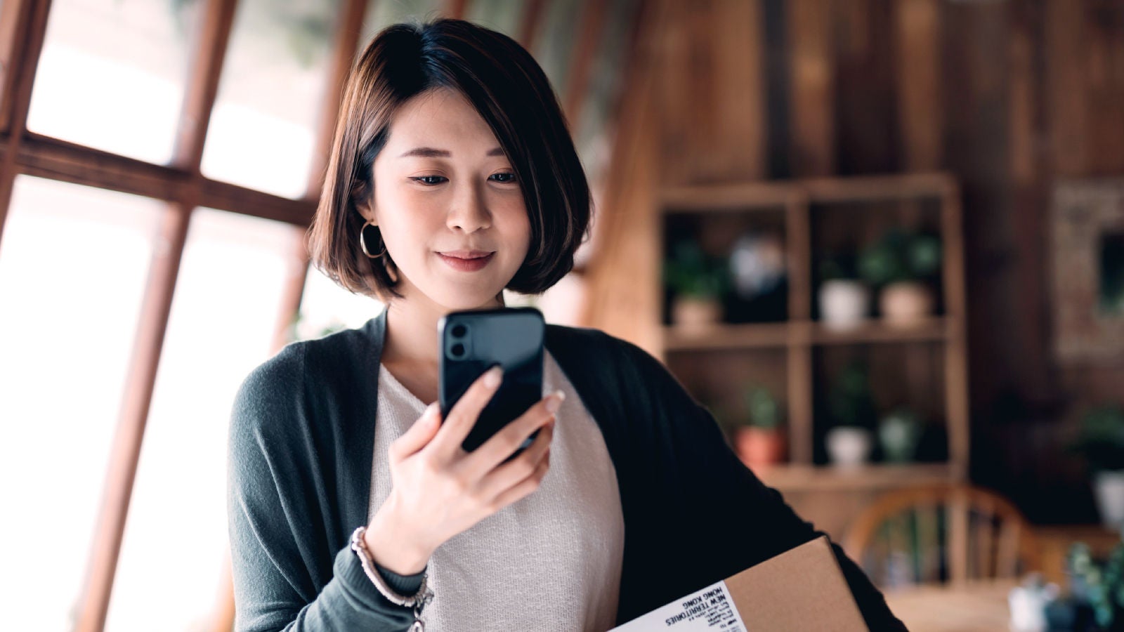 Woman looking at her cell phone holding a package