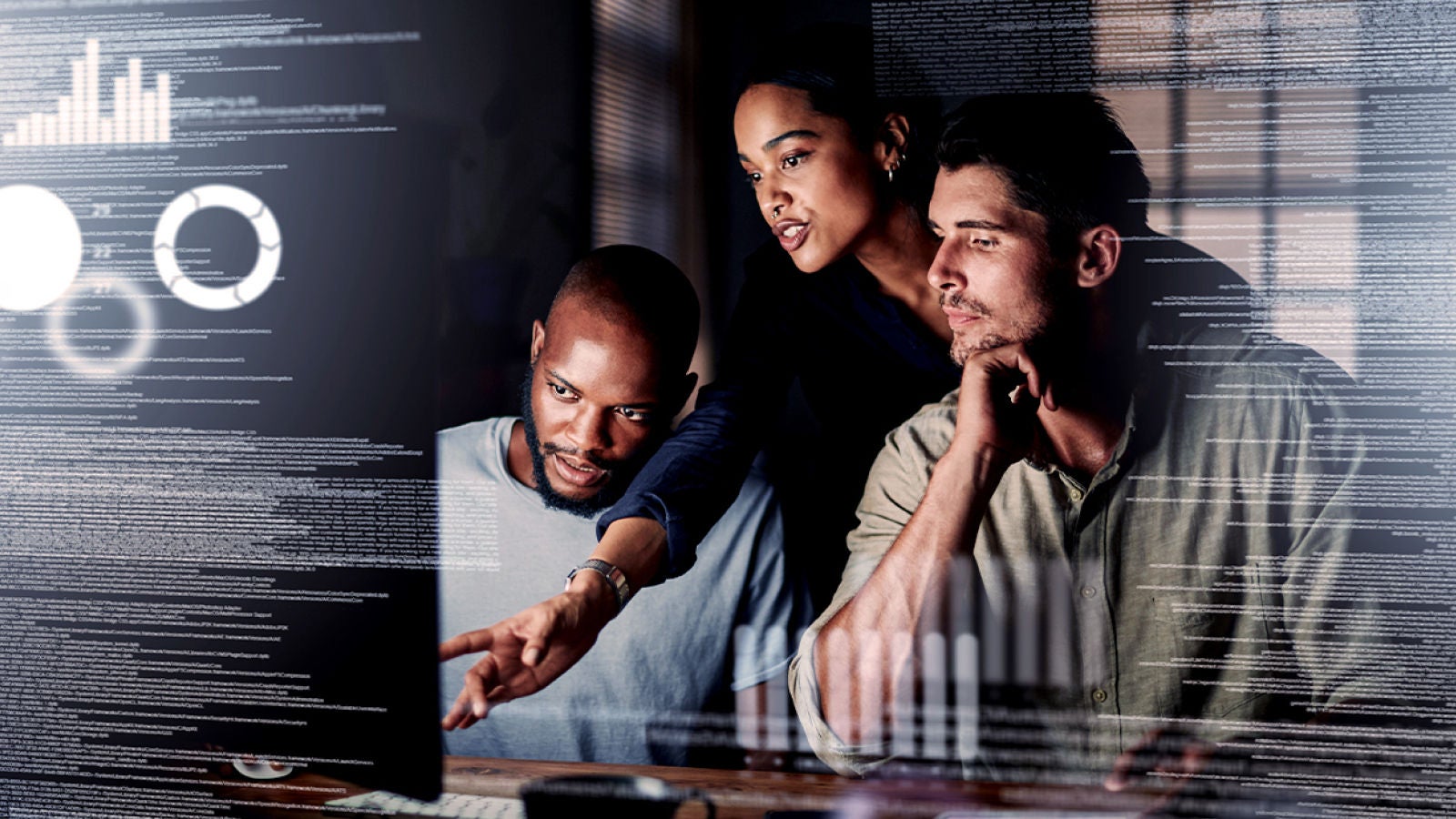 A team of three collaborating in front of a computer screen displaying digital analytics and data visualization.