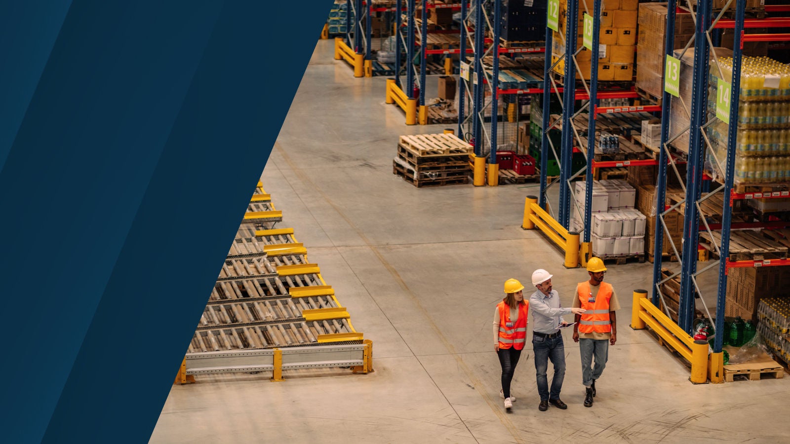 Three warehouse professionals wearing safety gear walk and discuss operations between storage racks and conveyor equipment.