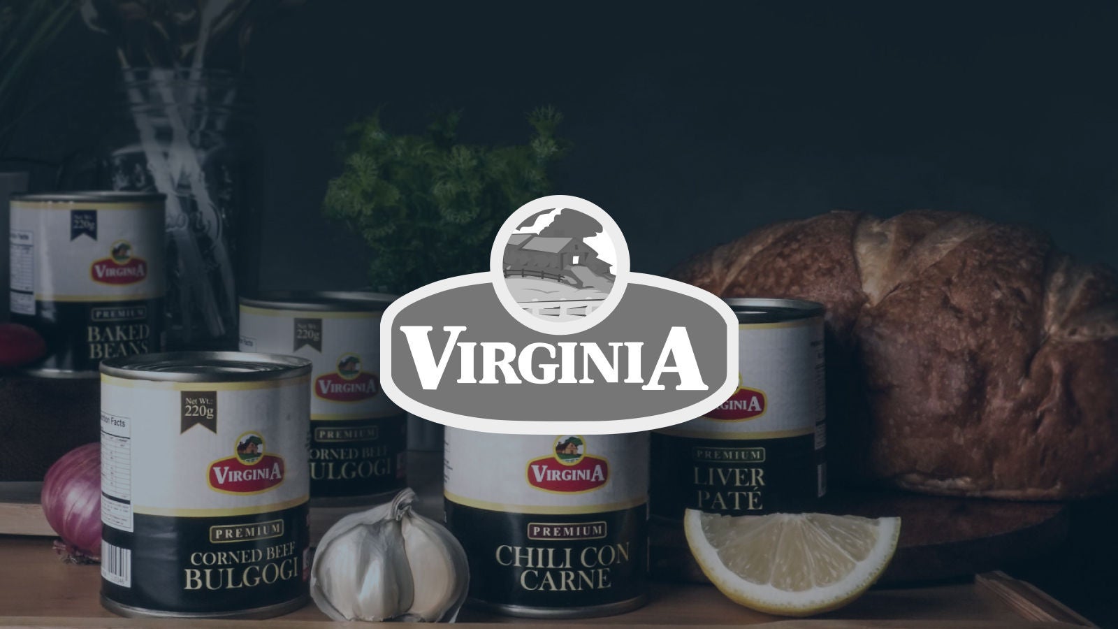 Assorted Virginia canned food products displayed with bread, garlic, onion, herbs, and a lemon wedge, with the Virginia logo centered over the scene.