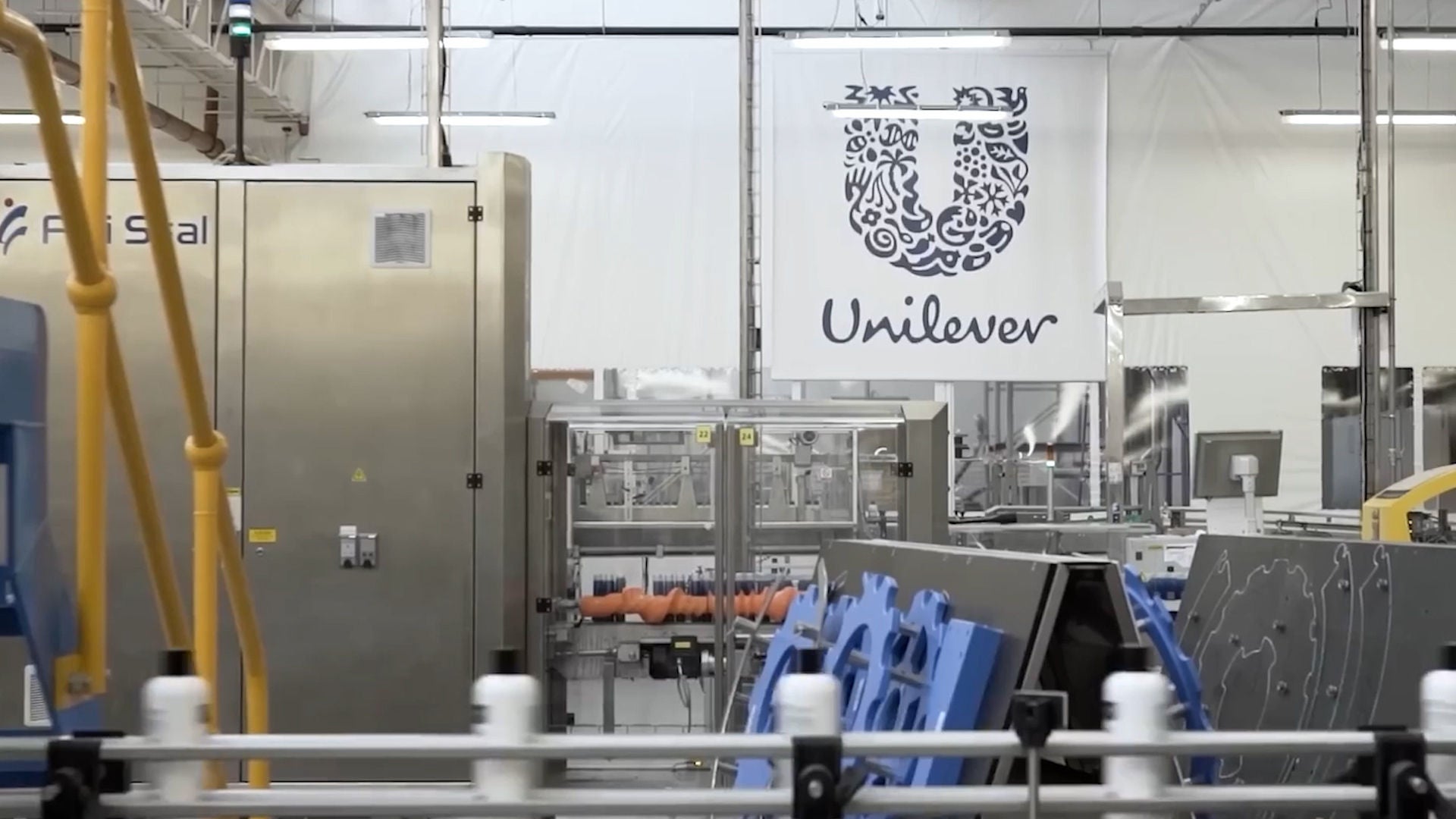 Manufacturing facility with production equipment and conveyor systems, featuring a large Unilever logo displayed above the production area.