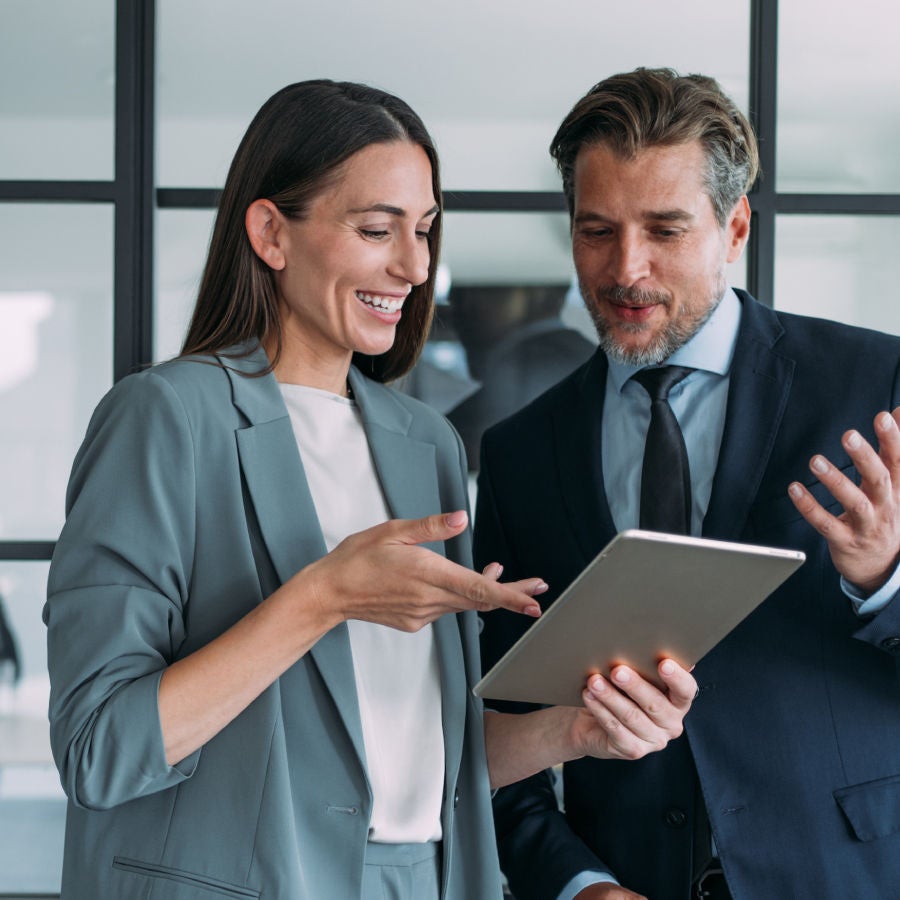 Two business professionals in suits and ties examine a tablet, engaged in a discussion or analysis of information.
