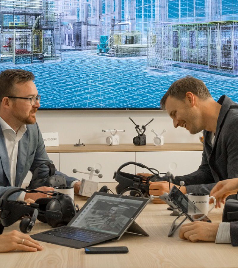 Autodesk team discussing a virtual model displayed on a screen, with VR headsets and digital tools on the table.