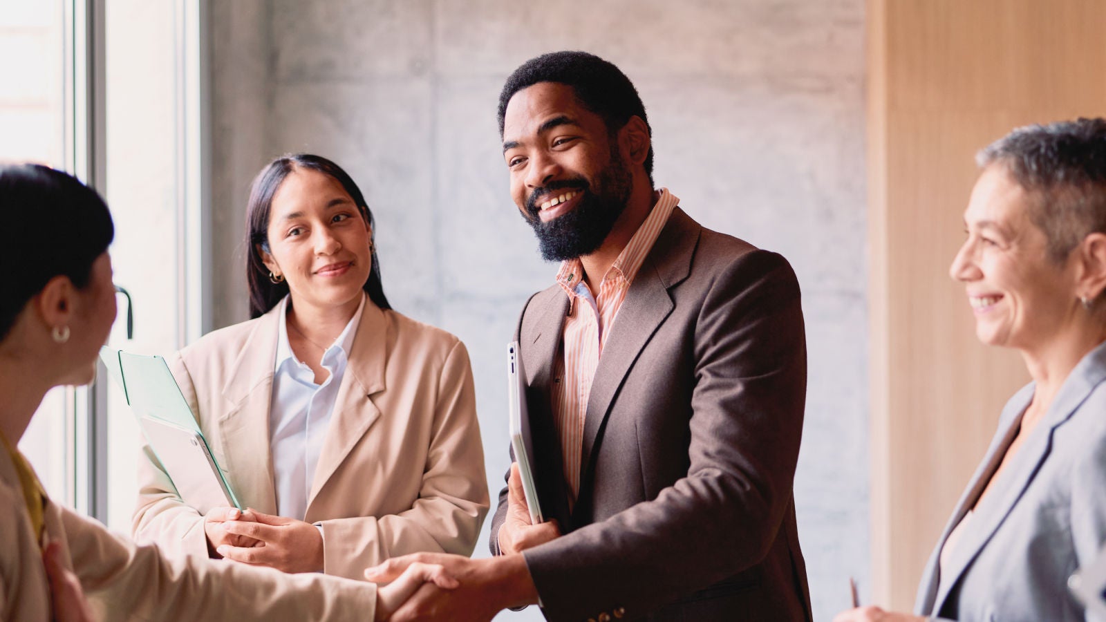 Business professionals smile during a meeting as one person shakes hands with a colleague.