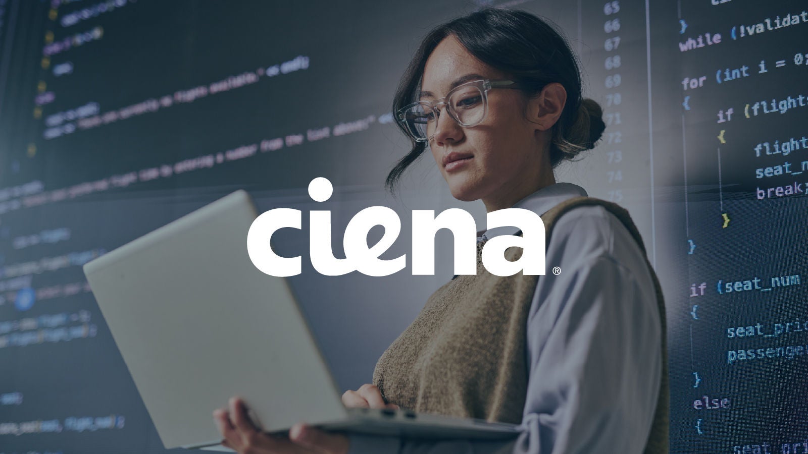 A professional holding a laptop while standing in front of a large screen displaying lines of code, with the Ciena logo overlaid.