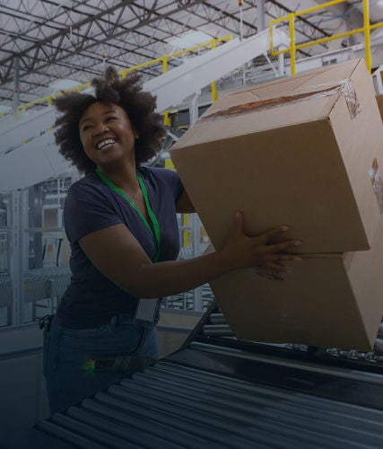 A warehouse worker lifting cardboard boxes onto a conveyor system in a distribution facility.