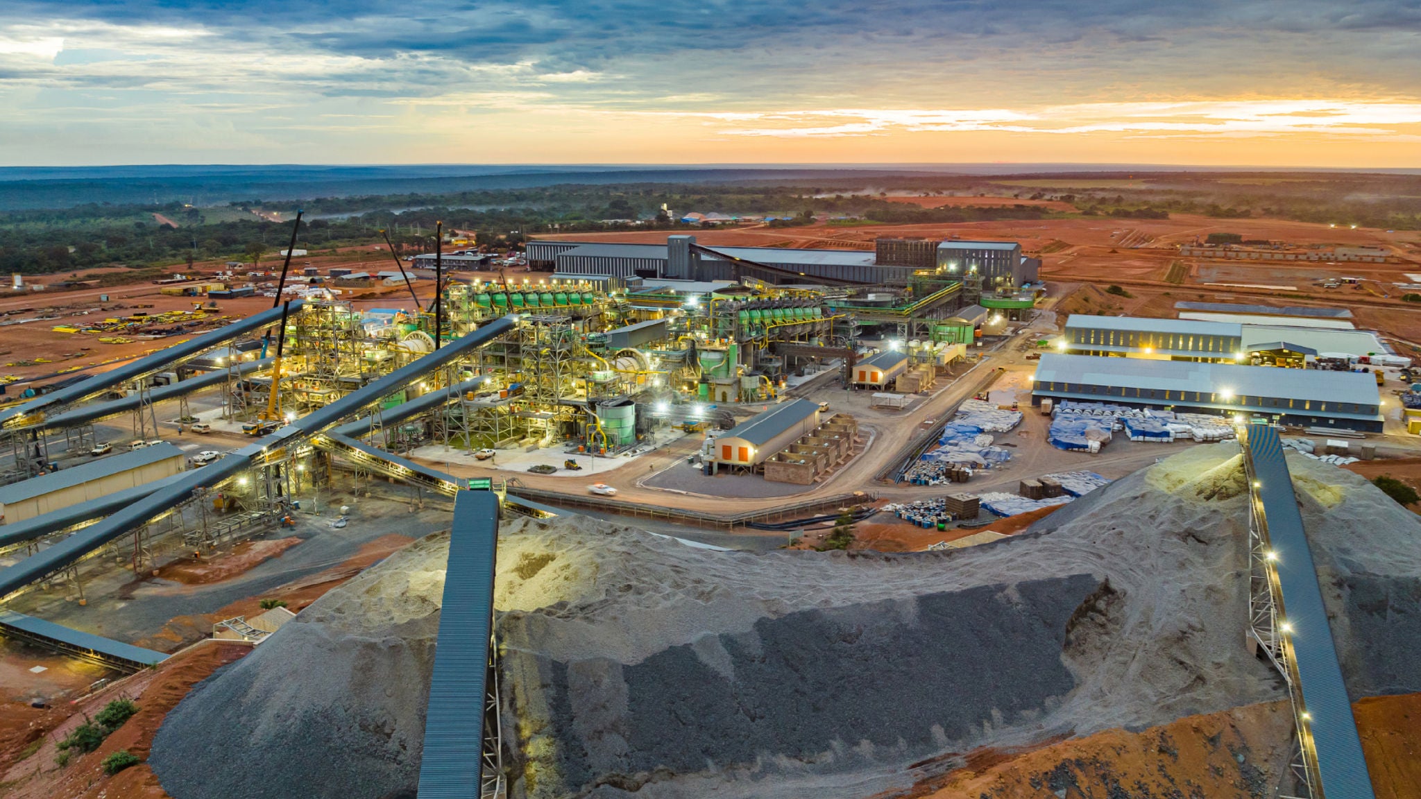 Large aerial view of the Kamoa Copper mining and processing facility with conveyor systems, industrial buildings, and surrounding landscape at sunset.