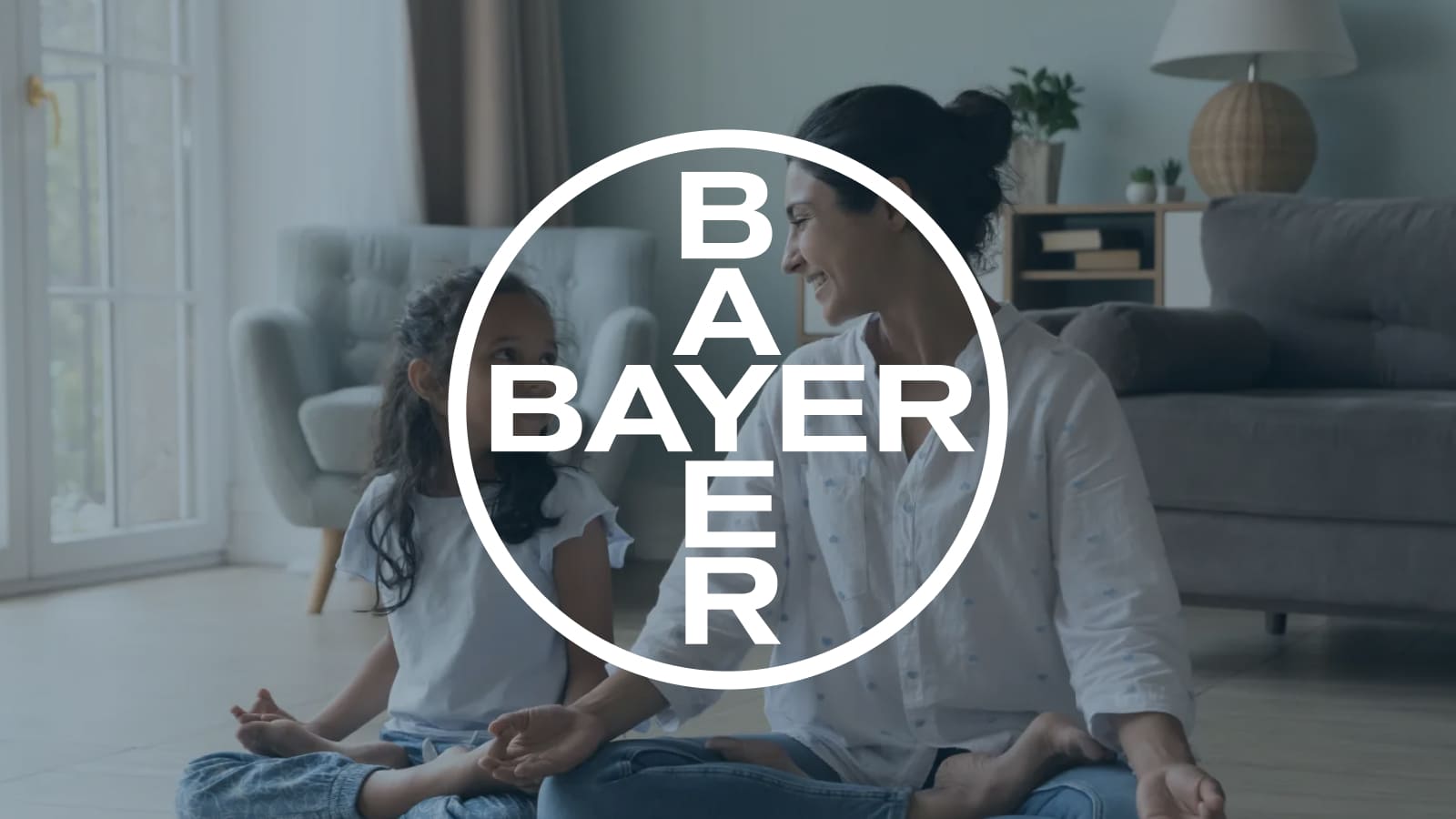 BAYER Logo displayed center. White circular logo over a woman and child sitting and smiling in a cozy living room.
